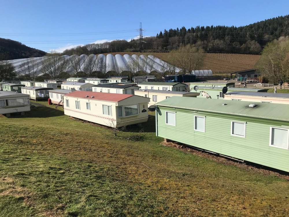 Seasonal worker accommodation at Cobrey Farm: rows of static homes (caravans) on grass, with polytunnels and Herefordshire hills in the background